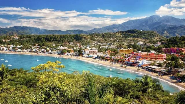 Panoramic view of Guayabitos bay with colorful beachfront hotels, turquoise water, and mountains
